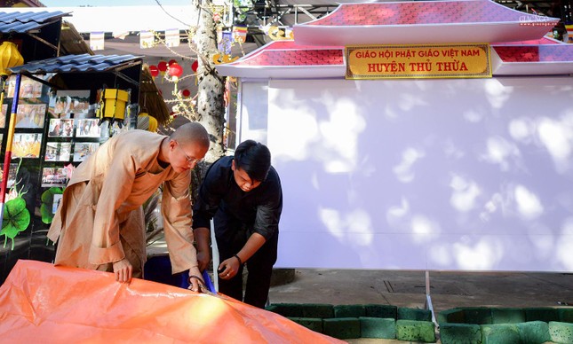 Một vị Tăng trẻ đang cùng Phật tử cắt tấm bạt để trang trí lễ đài Một vị Tăng trẻ đang cùng Phật tử cắt tấm bạt để trang trí lễ đài