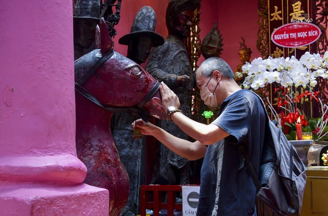 Một du khách đang thực hiện nghi thức lắc chuông cầu nguyện bình an trước bức tượng con ngựa bằng đá