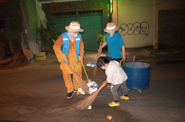 Một bạn nhỏ được phụ huynh hướng dẫn theo chân quý thầy, cô, chú quét rác làm sạch đường phố