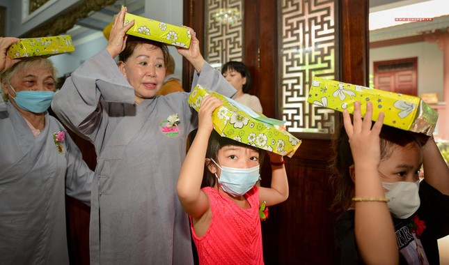 Một em nhỏ được mẹ hướng dẫn dâng pháp y cúng dường trong mùa Vu lan
