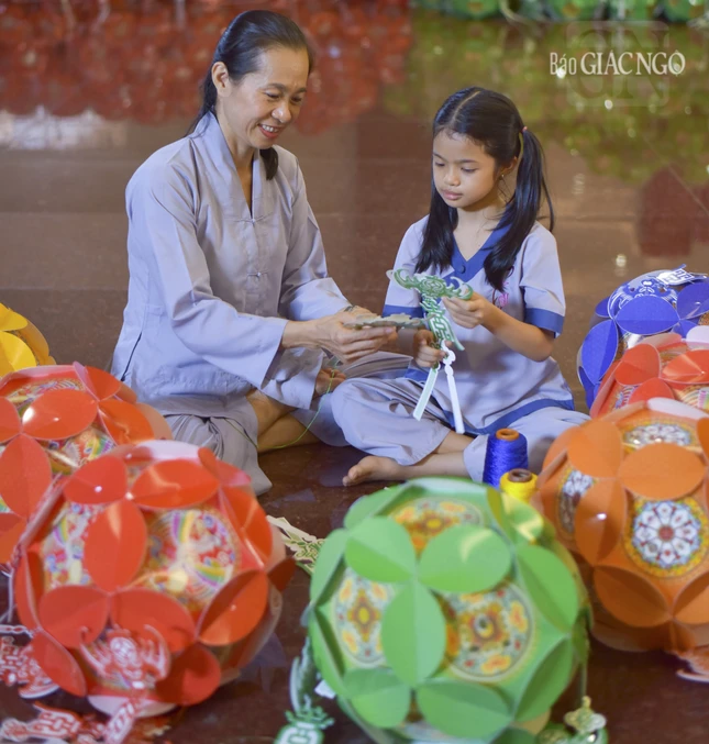 Bé Thanh Thảo chăm chú nghe mẹ hướng dẫn làm lồng đèn mừng Phật đản