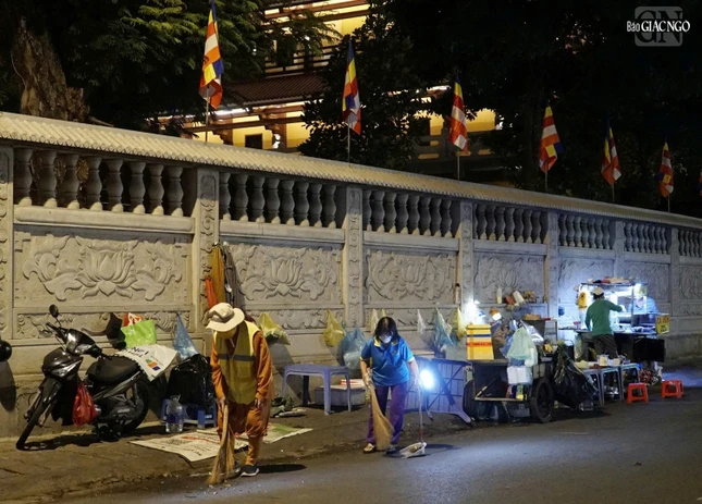 Hòa thượng Thích Duy Trấn cùng Phật tử rọi đèn để vệ sinh khu vực bên ngoài khuôn viên chùa, từ sáng sớm khi lát đát những quán hàng rong mới dọn hàng