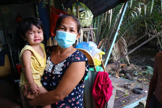 Chị Đặng Thị Thanh Hải, 42 tuổi, ẳm đứa con nhỏ 18 tháng tuổi bên căn nhà xập xệ cạnh con rạch ở gần bãi rác - Ảnh: Ngọc Trân