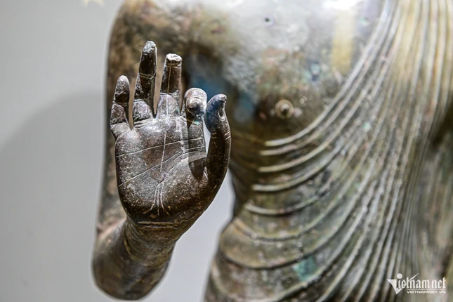 ... thân khoác áo cà sa, để hở vai phải, hai cánh tay đưa ra phía trước, tay phải với thủ ấn giảng pháp, tay trái nắm phần vạt áo choàng