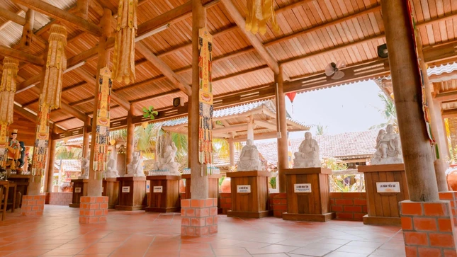 Hành lang dài với hàng cột gỗ dừa nâng đỡ mái ngói, hai bên đặt các tượng La-hán bằng đá trắng