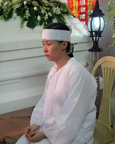 Khi không có ai, chị ngồi lặng lẽ, đơn độc bên quan tài chồng, nét mặt sầu thương.