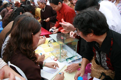 Từ sáng sớm, hàng nghìn người đã đổ về khu đúc tượng cạnh Học viện Phật giáo VN (Sóc Sơn, Hà Nội). Theo lịch âm, hôm nay là ngày "trùng cửu", ngày có ý nghĩa thiêng liêng đặc biệt, rất thích hợp để tiến hành đúc tượng Thánh Gióng - Đức Thánh Phù Đổng Thiên vương. Một mô hình thu nhỏ đặt cạnh khu đúc tượng để phật tử làm lễ, chiêm bái. Khi hoàn thành, tượng cao gần 11 m, độ vươn chéo lên trời khoảng 16 m. Rất nhiều người góp trang sức bằng kim loại quý để hòa cùng dòng đồng nóng chảy lúc đổ vào khuôn. Tại khu đất được cách ly cạnh đó, hai chiếc khuôn của phần đầu ngựa và thân trên Thánh Gióng đang gấp rút được hoàn tất những khâu cuối cùng. Đây là 2 thớt đầu tiên được đúc của tượng đài. Một số chi tiết khác của tượng đài cũng được làm trong mẻ đầu tiên. Hàng trăm thanh đồng đỏ nguyên chất được nung chảy trong lò ga hơn 1.000 độ C. Theo các nghệ nhân, thời gian từ lúc nấu đến lúc đổ đồng mất hơn 2 giờ. Người nghệ nhân cẩn thận trát kín mạch và tạo miệng khuôn để đổ đồng nóng chảy vào. Sau 2 giờ nung, mẻ đồng nóng chảy đổ ra... ...trong khi các nghệ nhân kính cẩn thắp hương mong mọi việc suôn sẻ. Bên ngoài hàng rào, hàng nghìn người chen lấn mong được vào chiêm ngưỡng cận cảnh. Tới dự buổi lễ sáng nay có nguyên Tổng bí thư Đỗ Mười, cùng nhiều vị lãnh đạo. Ngay trước thời khắc 9h9, hòa thượng Thích Thanh Tứ, Phó chủ tịch Trung ương hội Phật giáo VN(người đeo tràng hạt) cùng nhiều quan chức tiến vào khu đúc tượng. Hàng trăm món đồ kim loại quý được thả vào khuôn... ... trước khi dòng đồng đỏ nóng chảy được rót. Theo các nghệ nhân, công đoạn khó nhất của quá trình đúc tượng là khâu làm khuôn: mất 2 tháng. Khuôn phải làm sao để toát lên được thần thái của Thánh Gióng và toàn bộ hoa văn, họa tiết tinh xảo của tượng với đúng tỉ lệ 1:1. Sau khi đổ đầy đồng vào khuôn, cần tới 4 ngày để làm nguội tự nhiên rồi mới phá khuôn.