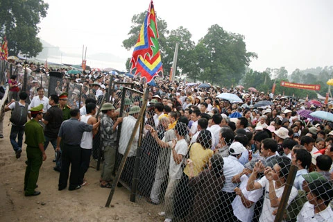 Từ sáng sớm, hàng nghìn người đã đổ về khu đúc tượng cạnh Học viện Phật giáo VN (Sóc Sơn, Hà Nội). Theo lịch âm, hôm nay là ngày "trùng cửu", ngày có ý nghĩa thiêng liêng đặc biệt, rất thích hợp để tiến hành đúc tượng Thánh Gióng - Đức Thánh Phù Đổng Thiên vương. Một mô hình thu nhỏ đặt cạnh khu đúc tượng để phật tử làm lễ, chiêm bái. Khi hoàn thành, tượng cao gần 11 m, độ vươn chéo lên trời khoảng 16 m. Rất nhiều người góp trang sức bằng kim loại quý để hòa cùng dòng đồng nóng chảy lúc đổ vào khuôn. Tại khu đất được cách ly cạnh đó, hai chiếc khuôn của phần đầu ngựa và thân trên Thánh Gióng đang gấp rút được hoàn tất những khâu cuối cùng. Đây là 2 thớt đầu tiên được đúc của tượng đài. Một số chi tiết khác của tượng đài cũng được làm trong mẻ đầu tiên. Hàng trăm thanh đồng đỏ nguyên chất được nung chảy trong lò ga hơn 1.000 độ C. Theo các nghệ nhân, thời gian từ lúc nấu đến lúc đổ đồng mất hơn 2 giờ. Người nghệ nhân cẩn thận trát kín mạch và tạo miệng khuôn để đổ đồng nóng chảy vào. Sau 2 giờ nung, mẻ đồng nóng chảy đổ ra... ...trong khi các nghệ nhân kính cẩn thắp hương mong mọi việc suôn sẻ. Bên ngoài hàng rào, hàng nghìn người chen lấn mong được vào chiêm ngưỡng cận cảnh. Tới dự buổi lễ sáng nay có nguyên Tổng bí thư Đỗ Mười, cùng nhiều vị lãnh đạo. Ngay trước thời khắc 9h9, hòa thượng Thích Thanh Tứ, Phó chủ tịch Trung ương hội Phật giáo VN(người đeo tràng hạt) cùng nhiều quan chức tiến vào khu đúc tượng. Hàng trăm món đồ kim loại quý được thả vào khuôn... ... trước khi dòng đồng đỏ nóng chảy được rót. Theo các nghệ nhân, công đoạn khó nhất của quá trình đúc tượng là khâu làm khuôn: mất 2 tháng. Khuôn phải làm sao để toát lên được thần thái của Thánh Gióng và toàn bộ hoa văn, họa tiết tinh xảo của tượng với đúng tỉ lệ 1:1. Sau khi đổ đầy đồng vào khuôn, cần tới 4 ngày để làm nguội tự nhiên rồi mới phá khuôn.