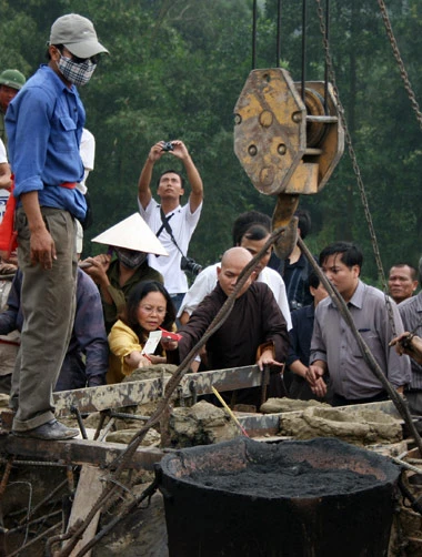 Từ sáng sớm, hàng nghìn người đã đổ về khu đúc tượng cạnh Học viện Phật giáo VN (Sóc Sơn, Hà Nội). Theo lịch âm, hôm nay là ngày "trùng cửu", ngày có ý nghĩa thiêng liêng đặc biệt, rất thích hợp để tiến hành đúc tượng Thánh Gióng - Đức Thánh Phù Đổng Thiên vương. Một mô hình thu nhỏ đặt cạnh khu đúc tượng để phật tử làm lễ, chiêm bái. Khi hoàn thành, tượng cao gần 11 m, độ vươn chéo lên trời khoảng 16 m. Rất nhiều người góp trang sức bằng kim loại quý để hòa cùng dòng đồng nóng chảy lúc đổ vào khuôn. Tại khu đất được cách ly cạnh đó, hai chiếc khuôn của phần đầu ngựa và thân trên Thánh Gióng đang gấp rút được hoàn tất những khâu cuối cùng. Đây là 2 thớt đầu tiên được đúc của tượng đài. Một số chi tiết khác của tượng đài cũng được làm trong mẻ đầu tiên. Hàng trăm thanh đồng đỏ nguyên chất được nung chảy trong lò ga hơn 1.000 độ C. Theo các nghệ nhân, thời gian từ lúc nấu đến lúc đổ đồng mất hơn 2 giờ. Người nghệ nhân cẩn thận trát kín mạch và tạo miệng khuôn để đổ đồng nóng chảy vào. Sau 2 giờ nung, mẻ đồng nóng chảy đổ ra... ...trong khi các nghệ nhân kính cẩn thắp hương mong mọi việc suôn sẻ. Bên ngoài hàng rào, hàng nghìn người chen lấn mong được vào chiêm ngưỡng cận cảnh. Tới dự buổi lễ sáng nay có nguyên Tổng bí thư Đỗ Mười, cùng nhiều vị lãnh đạo. Ngay trước thời khắc 9h9, hòa thượng Thích Thanh Tứ, Phó chủ tịch Trung ương hội Phật giáo VN(người đeo tràng hạt) cùng nhiều quan chức tiến vào khu đúc tượng. Hàng trăm món đồ kim loại quý được thả vào khuôn... ... trước khi dòng đồng đỏ nóng chảy được rót. Theo các nghệ nhân, công đoạn khó nhất của quá trình đúc tượng là khâu làm khuôn: mất 2 tháng. Khuôn phải làm sao để toát lên được thần thái của Thánh Gióng và toàn bộ hoa văn, họa tiết tinh xảo của tượng với đúng tỉ lệ 1:1. Sau khi đổ đầy đồng vào khuôn, cần tới 4 ngày để làm nguội tự nhiên rồi mới phá khuôn.