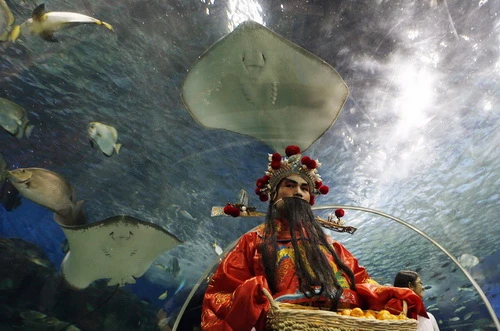 Một nhân viên trong trang phục Thần tài cầm rổ kẹo bánh, hoa quả tặng người qua lại ở công viên Ocean (Manila, Philippines) - Ảnh: Reuters