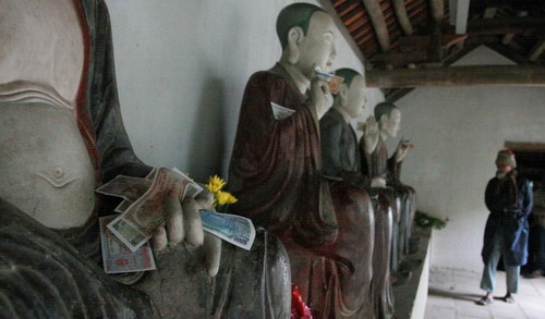 18 vị La Hán cơ mà, các khách "tín ngưỡng" thoải mái nhét tiền cầu may! Cô nàng cầm cả tập tiền lẻ dày cộp, vái đến chóng mặt, giắt tiền vào ngai tượng Thập bát (18) vị La Hán chùa Mía được nhiều tài liệu cho rằng còn đẹp hơn cả “Các vị La Hán chùa Tây Phương” về giá trị thẩm mỹ, điêu khắc cổ. Mỗi người một vẻ, nhưng, tất cả đều bị khách đi chùa “ép” phải cấm tiền lẻ như thế này.