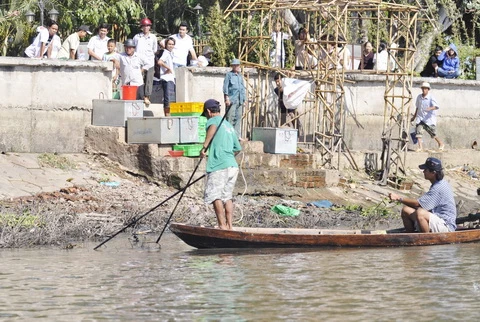 Trong khi đó, hai người này ra sức dùng dụng cụ đánh bắt bằng điện gom cá trước sự chứng kiến của những người chuẩn bị mua cá phóng sinh - Ảnh: Mai Vinh