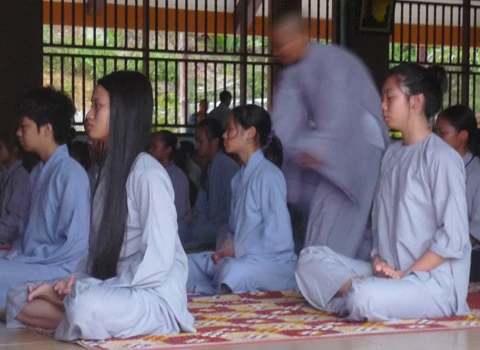 Hơn 600 học sinh tề tựu trong lễ khai giảng. Buổi học thiền đầu tiên. Không giấu nổi sự hồn nhiên. Cùng nhau xuống núi đi khất thực. Cười hồn nhiên trong giờ tiểu thực. Tập trung trở lại khu nhà ở sau giờ ăn trưa. Sư thầy nhẹ nhàng nhắc nhở các em nhỏ đi đúng hàng. Hai em nhỏ tranh thủ giờ nghỉ trưa xem lại bài vở. Các em cùng nhau học Phật pháp. Vốn là nơi tu hành của các bậc chư tăng, song để đáp ứng nhu cầu chúng sinh, Thiền viện Trúc Lâm Tây Thiên đã nhận giúp các "cậu ấm, cô chiêu" tập tu, sửa mình mà không thu bất cứ khoản lệ phí nào. Lớp học năm trước chỉ có 40-50 em nhỏ, do tiếng lành đồn xa, năm nay con số đã gấp hơn 10 lần. Các thầy phải chia làm nhiều khóa học để tiếp nhận các em. Khóa học đầu tiên dành cho các em từ 10 đến 14 tuổi, khai giảng vào ngày 13/6 và sẽ kết thúc sau 2 tuần. Thiền sư Thích Kiến Nguyệt, trụ trì Thiền viện Trúc Lâm Tây Thiên cho biết, do khuôn viên và số lượng thiền sư có hạn nên không thể nhận cùng lúc tất cả em nhỏ. Hiện 90 thầy, cô phải làm việc hết mình để quản lý, dạy dỗ 600 em nhỏ. Nói về lợi ích của việc tu tập, đặc biệt là ngồi thiền, thầy Nguyệt nhận xét: “Thiền là phương pháp tĩnh tâm khai trí. Khoa học đã chứng minh đứa trẻ ngồi thiền thông minh, kiên nhẫn hơn những đứa trẻ không ngồi thiền. Hiện nay, ở nhiều nước đã đưa thiền vào chương trình giáo dục. Các em tranh thủ đọc sách Phật trong giờ nghỉ. Ảnh: Hải Đăng. Ngoài việc học thiền, các sư thầy, sư cô sẽ chỉ dạy cho các em thói quen thức dậy từ 3h sáng, gập chăn màn sao cho vuông vức, ngay ngắn, sau đó nhẹ nhàng di chuyển về giảng đường để tọa thiền. Kết thúc giờ tọa thiền lúc 5h sáng, các em sẽ đến với bữa sáng gọi là tiểu thực. Lũ trẻ tay cầm bát, xếp thành hàng dài ngay ngắn đi về phía Trai đường để tự chọn khẩu phần ăn chay cho mình. 7h30 là bắt đầu giờ học đạo. Các em nhỏ được dạy kinh Phật để biết nhìn vạn vật bằng tình yêu thương, biết đúng, biết sai để sớm "phát tâm tỉnh giác, xa lìa chỗ tối tăm". 11h trưa là đến giờ khất thực (ăn trưa). Trước khi ăn, lũ trẻ phải chắp tay cầu nguyện và cùng nghe thầy giảng về nguồn gốc hạt lúa, củ khoai, ý nghĩa của những bữa ăn chay... Buổi chiều những cậu ấm, cô chiêu vốn quen với nếp sống thị thành, quen với sự nuông chiều, ỉ lại vào cha mẹ, người thân, được dạy cách làm việc nhà như: nấu cơm bằng bếp củi, rửa bát, nhặt rau... Các em kết thúc một ngày bằng lễ sám hối tại chánh điện, tức là xem xét lại tất cả những hành động trong ngày để nhận biết đúng, sai và sửa mình. Có nhiều lý do để các bậc phụ huynh đưa con em đến tập tu. Người thì muốn con tách khỏi cuộc sống thường nhật để cai games, người muốn con được học Phật pháp để chúng hiểu rõ hơn về ý nghĩa cuộc sống, trân trọng những gì đang có, để chúng biết được nguồn gốc của hạt lúa, củ khoai, biết trân trọng thành quả lao động của người khác. Và cũng có những ông bố bà mẹ đưa con lên chỉ để con biết thế nào là nhặt rau, quét nhà, nấu cơm… Chia sẻ cảm giác về ngày đầu tập tu, cô bé Phạm Phương Thảo, 14 tuổi, thật thà: “Cháu chẳng muốn lên đây, ở đây chán lắm, chẳng qua là bố mẹ ép. Cháu nghiện Audition nặng, chỉ cần hai chai nước, chẳng cần ăn gì, cháu có thể ngồi cả ngày. Giờ này bọn bạn cháu chắc đang ngồi ở quán net đầu đường Tô Hiệu (Cầu Giấy, Hà Nội)". Khác với sự bạo dạn của Thảo, hai chị em Nguyễn Việt Hà (14 tuổi) và Nguyễn Việt Hương (6 tuổi) ở Đống Đa (Hà Nội) tỏ ra dè dặt khi tiếp xúc với người lạ. Hương nhỏ tuổi nhất tại khóa học lần này. Thấy bố mẹ đưa chị lên đây để có thời gian nghỉ ngơi sau một năm học vất vả, cô bé nhất định đòi lên cùng chị. Đôi mắt sưng húp, Hà nói: “Hết giờ sám hối chiều qua, em cháu bắt đầu khóc đòi mẹ. Các cô dỗ mãi nó mới chịu nín. 11h đêm nó lại khóc, thế là cả phòng cháu khóc theo. Cháu nhớ nhà lắm. Cho cháu mượn điện thoại để gọi về cho mẹ được không?”. Được mượn điện thoại, cô bé vừa bấm số gọi cho mẹ vừa nước mắt lưng tròng. Cô chị ôm lấy cô em, thút thít nói chuyện với mẹ… Một em trai cũng không cầm được nước mắt vì nhớ nhà. Ảnh: Hải Đăng. Phía ngoài bậc thang bước lên giảng đường, hai ni cô cũng ra sức dỗ dành cậu bé Bùi Công Huy (10 tuổi) ở Hà Giang đang đòi về. Huy vừa khóc vừa nói: “Cháu không quen ăn chay, nhạt lắm. Ở đây cháu còn phải tự gập quần áo, nấu cơm, rửa bát, đến giờ ăn còn phải tự bưng bát, xếp hàng xới cơm… Cháu không quen, cháu muốn về với mẹ”. Các em lớn thì tỏ ra cứng rắn và thích nghi nhanh hơn với nếp sống tại thiền viện. Khuôn mặt tuấn tú, đeo kính cận, cậu bé Phan Thành Hưng (16 tuổi) ở phường Bách Khoa, Hà Nội, nhẹ nhàng lật giở quyển kinh. “Đây là lần thứ hai em lên thiền viện. Năm ngoái vì quá nghiện Internet nên bố mẹ đưa em lên. Năm nay, nghỉ hè là em xin bố mẹ lên luôn. Bây giờ em đã quen với việc ăn chay, dậy sớm từ 3h sáng, tự xúc khẩu phần ăn cho mình, tự rửa bát, quét nhà. Các thầy, các cô chỉ bảo ân cần lắm”, Hưng chia sẻ. Bóng chiều buông xuống, anh Quách Ngọc Huy (Tây Hồ, Hà Nội) đang chuẩn bị chia tay hai cô con gái để về Hà Nội. "Tôi có 3 con gái và muốn cả ba cháu lên đây nhưng vì cháu út mới 4 tuổi nên đành phải ở nhà với mẹ. Thú thật lên đây tôi thấy không khí thật thanh bình. Nhìn thấy con tự rửa bát, quét nhà mà tôi mừng quá. Ở nhà chúng có biết làm gì đâu. Tôi mong nhà chùa mở thêm nhiều khóa học như thế này để các em có được một học kỳ 3 thật hữu ích", anh Huy nói. 18h30 chiều, mặt trời đỏ lự phía sau mái chùa cong cong. Hàng thông reo vi vu. Phía nhà dân dưới chân núi, mấy cột khói bếp mịt mùng hòa vào khói lam chiều. Trên giảng đường ở thiền viện, đám trẻ nghiêm trang chắp tay trước tượng Phật và cầu nguyện theo các thầy để chúng sinh “xa rời đường dữ”, được ấm no, hạnh phúc.