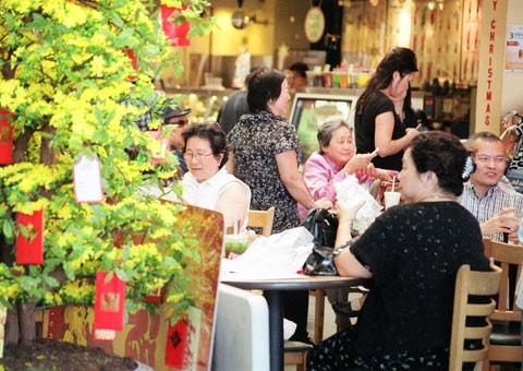 Khách ngồi ăn uống tại tiệm Lee Sandwich bên trong Phước Lộc Thọ. Bên ngoài tiệm ăn là cây cảnh được treo đầy phong bao đỏ.