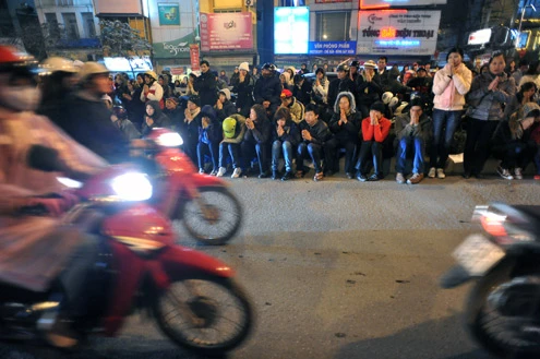 Cảnh đội mưa ngồi kín mít dài gần cây số tại tuyến đường Tây Sơn, gần Tổ đình Phúc Khánh lúc 19h tối 14/1 âm lịch Giao thông tắc nghẽn kéo dài trên tuyến đường này và một số phố giao nối Nhiều người che chắn tập thể bằng một tấm nylon dài, người chưa chuẩn bị đành ngồi đội mưa Tết Nguyên tiêu là ngày lễ thiêng đầu năm mới. Tục truyền, trong ngày rằm tháng Giêng, Đức Phật giáng lâm tại các chùa để chứng giám lòng thành của tín đồ Do đó ngày 14 hoặc chính rằm tháng Giêng, các đền, chùa trở nên quá tải. Tại Hà Nội, chùa Phúc Khánh nổi tiếng là nơi linh thiêng nhất nên thu hút rất đông người dân tới cầu phúc, cầu an Một trong những em bé theo mẹ đến ngồi hàng tiếng đồng hồ trên xe máy trong giá lạnh ngoài phố chờ làm lễ Dải phân cách tại lối lên cầu vượt Ngã Tư Sở cũng chật kín Một cô gái lặng lẽ mặc áo mưa, tay đi găng lầm rầm khấn vái Đứng tràn cả ra lòng đường, cậu thiếu niên này cũng chắp tay làm lễ như người lớn Hết giờ, ghế được giơ cao trên đầu trên đường về Niềm vui sau khi lễ bái thành công và được phát lộc của một người đàn ông Báo, giấy lót chỗ ngồi xả bừa bãi khiến tuyến đường tràn ngập rác