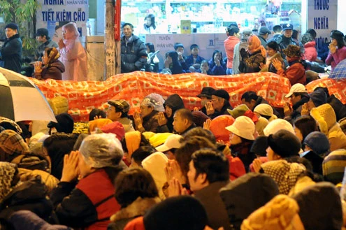 Cảnh đội mưa ngồi kín mít dài gần cây số tại tuyến đường Tây Sơn, gần Tổ đình Phúc Khánh lúc 19h tối 14/1 âm lịch Giao thông tắc nghẽn kéo dài trên tuyến đường này và một số phố giao nối Nhiều người che chắn tập thể bằng một tấm nylon dài, người chưa chuẩn bị đành ngồi đội mưa Tết Nguyên tiêu là ngày lễ thiêng đầu năm mới. Tục truyền, trong ngày rằm tháng Giêng, Đức Phật giáng lâm tại các chùa để chứng giám lòng thành của tín đồ Do đó ngày 14 hoặc chính rằm tháng Giêng, các đền, chùa trở nên quá tải. Tại Hà Nội, chùa Phúc Khánh nổi tiếng là nơi linh thiêng nhất nên thu hút rất đông người dân tới cầu phúc, cầu an Một trong những em bé theo mẹ đến ngồi hàng tiếng đồng hồ trên xe máy trong giá lạnh ngoài phố chờ làm lễ Dải phân cách tại lối lên cầu vượt Ngã Tư Sở cũng chật kín Một cô gái lặng lẽ mặc áo mưa, tay đi găng lầm rầm khấn vái Đứng tràn cả ra lòng đường, cậu thiếu niên này cũng chắp tay làm lễ như người lớn Hết giờ, ghế được giơ cao trên đầu trên đường về Niềm vui sau khi lễ bái thành công và được phát lộc của một người đàn ông Báo, giấy lót chỗ ngồi xả bừa bãi khiến tuyến đường tràn ngập rác