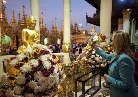 Ngoại trưởng Mỹ đặt hoa trước một pho tượng Phật dát vàng trong chùa Shwedagon, phía xa là một dãy tháp dát vàng. Ảnh: AFP