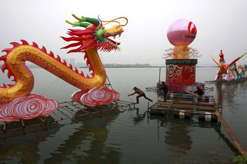 Các công nhân đang lắp đặt đèn lồng khổng lồ hình con rồng trên một hồ nước để chào đón năm mới Âm lịch ở Suining, tỉnh Tứ Xuyên. Năm mới cổ truyền ở Trung Quốc sẽ bắt đầu từ ngày 23/1 Dương lịch. Những người đàn ông Trung Quốc múa rồng trên một hồ nước đóng băng chào đón năm mới ở Shenyang, tỉnh Liêu Ninh ngày 1/1/2012. Thợ lặn múa rồng trong một sự kiện chào đón năm mới Âm lịch ở trong một bể cá tại Bắc Kinh ngày 5/1/2012. Công nhân trang trí một bức tượng hình con rồng để chuẩn bị cho một sự kiện chào đón năm mới cổ truyền ở Ôn Châu, Chiết Giang ngày 9/1. Một công nhân xịt sơn cho bộ phận của chiếc đèn lồng hình người, để chuẩn bị cho một sự kiện chào đón năm mới ở Suining, Tứ Xuyên. Công nhân đang lắp đặt một đèn lồng hình rồng ở trên tường ở Nam Kinh. Du khách chụp hình chiếc đèn lồng hình rồng rực sáng trong đêm ở Bắc Kinh ngày 7/1. Người mẫu đội một chiếc mũ làm từ chocolate, tại sự kiện Chocolate Thế giới ở Thượng Hải để chào đón năm mới. Học sinh cầm câu đối, đèn lồng và múa rồng để chào đóng năm mới tại một ngôi trường tiểu học tại Cửu Giang, Giang Tây. Công nhân nhập cư dùng bữa tại một công trường ở Thành Đô, Trung Quốc ngày 9/1. Hơn 1.400 công nhân nhập cư đã tham gia bữa ăn thường niên để chào mừng năm mới. Đèn lồng trang hoàng rực rỡ tại một con phố ở Zibo, Trung Quốc ngày 8/1. Công nhân đang dựng một bức tượng hình Quan Âm trên những chiếc đèn lồng hình rồng ở Tứ Xuyên ngày 7/1. Một giáo viên đang cho các học sinh xem bức tranh hình rồng ở một ngôi trường tiểu học tại tỉnh Sơn Đông ngày 5/1. Người đàn ông giơ bức thư có gắn tem hình rồng tại Huaibei, tỉnh An Huy ngày 5/1. Tem thư được thiết kế có hình rồng này đã gây ra sự chỉ trích của người dân, khi họ cho rằng con rồng này có hình dáng quá hung tợn.