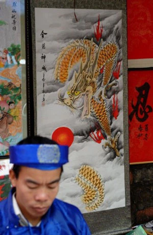 Một nghệ nhân thư pháp đang viết chữ cho khách, phía sau là bức tranh hình rồng rất đẹp được treo trên bức tường của Văn Miếu Quốc Tử Giám ở Hà Nội. Ảnh: AFP