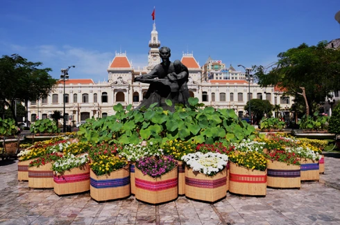 Sau những tuyến đường lớn như Đồng Khởi, Lê Duẩn, Lê Lợi, một số phố khác ở trung tâm thành phố cũng hoàn thành việc trang trí Tết. Đây là năm mà TP HCM có nhiều tuyến được thắp sáng bằng các dải đèn màu, theo từng chủ đề khác nhau. Thương xá Tax năm nay lấy màu hoa mai làm chủ đạo với ánh đèn đỏ, ấm vàng. Bên dưới là các trang trí Tết, từ 18h, rất đông người đến chụp ảnh và ngắm không khí xuân. Trong khi đó, từ các cửa hiệu lớn... ... đến các trung tâm thương mại, khách sạn bắt đầu trang trí bằng ánh sáng đủ màu. Đường hoa Nguyễn Huệ đang bước vào những ngày cuối cùng trước khi khai mạc sáng 27 tháng Chạp. Các biểu tượng năm rắn và quê hương đất nước đã gần hoàn thành. Những công nhân đang tưới các giò hoa treo cao. Mỗi chủ đề trên con đường hoa năm nay được dàn dựng bằng các hình ảnh mang cảnh sắc quen thuộc của Việt Nam. Rặng tre, ruộng lúa và khóm hoa xuất hiện giữa đường. Nhiều tuyến phố trung tâm thành phố được trang trí bằng đủ các loại hoa sặc sỡ. Tượng đài Hồ Chủ tịch trước UBND thành phố với sen chủ đạo và các cánh hoa màu sắc khác nhau. Các con thuyền hoa bên cạnh hồ Bán nguyệt, quận 7. Các hội chợ, lễ hội hoa đã diễn ra từ ngày 23 tháng Chạp. Năm nay, hoa từ các tỉnh miền Tây và phía Bắc chuyển về nhiều, mức giá vừa phải. Trong những ngày đầu mở cửa, lượng khách vãn cảnh nhiều, nhưng người mua ít.