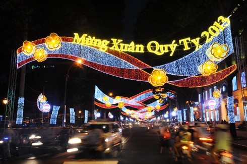 Sau những tuyến đường lớn như Đồng Khởi, Lê Duẩn, Lê Lợi, một số phố khác ở trung tâm thành phố cũng hoàn thành việc trang trí Tết. Đây là năm mà TP HCM có nhiều tuyến được thắp sáng bằng các dải đèn màu, theo từng chủ đề khác nhau. Thương xá Tax năm nay lấy màu hoa mai làm chủ đạo với ánh đèn đỏ, ấm vàng. Bên dưới là các trang trí Tết, từ 18h, rất đông người đến chụp ảnh và ngắm không khí xuân. Trong khi đó, từ các cửa hiệu lớn... ... đến các trung tâm thương mại, khách sạn bắt đầu trang trí bằng ánh sáng đủ màu. Đường hoa Nguyễn Huệ đang bước vào những ngày cuối cùng trước khi khai mạc sáng 27 tháng Chạp. Các biểu tượng năm rắn và quê hương đất nước đã gần hoàn thành. Những công nhân đang tưới các giò hoa treo cao. Mỗi chủ đề trên con đường hoa năm nay được dàn dựng bằng các hình ảnh mang cảnh sắc quen thuộc của Việt Nam. Rặng tre, ruộng lúa và khóm hoa xuất hiện giữa đường. Nhiều tuyến phố trung tâm thành phố được trang trí bằng đủ các loại hoa sặc sỡ. Tượng đài Hồ Chủ tịch trước UBND thành phố với sen chủ đạo và các cánh hoa màu sắc khác nhau. Các con thuyền hoa bên cạnh hồ Bán nguyệt, quận 7. Các hội chợ, lễ hội hoa đã diễn ra từ ngày 23 tháng Chạp. Năm nay, hoa từ các tỉnh miền Tây và phía Bắc chuyển về nhiều, mức giá vừa phải. Trong những ngày đầu mở cửa, lượng khách vãn cảnh nhiều, nhưng người mua ít.