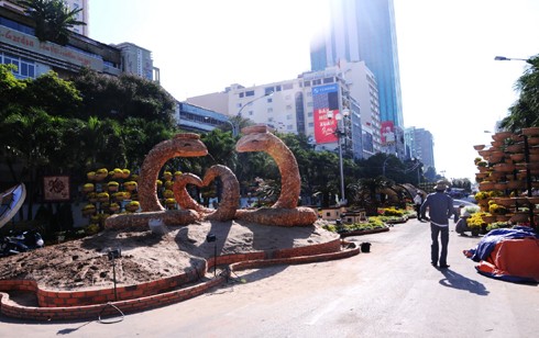 Sau những tuyến đường lớn như Đồng Khởi, Lê Duẩn, Lê Lợi, một số phố khác ở trung tâm thành phố cũng hoàn thành việc trang trí Tết. Đây là năm mà TP HCM có nhiều tuyến được thắp sáng bằng các dải đèn màu, theo từng chủ đề khác nhau. Thương xá Tax năm nay lấy màu hoa mai làm chủ đạo với ánh đèn đỏ, ấm vàng. Bên dưới là các trang trí Tết, từ 18h, rất đông người đến chụp ảnh và ngắm không khí xuân. Trong khi đó, từ các cửa hiệu lớn... ... đến các trung tâm thương mại, khách sạn bắt đầu trang trí bằng ánh sáng đủ màu. Đường hoa Nguyễn Huệ đang bước vào những ngày cuối cùng trước khi khai mạc sáng 27 tháng Chạp. Các biểu tượng năm rắn và quê hương đất nước đã gần hoàn thành. Những công nhân đang tưới các giò hoa treo cao. Mỗi chủ đề trên con đường hoa năm nay được dàn dựng bằng các hình ảnh mang cảnh sắc quen thuộc của Việt Nam. Rặng tre, ruộng lúa và khóm hoa xuất hiện giữa đường. Nhiều tuyến phố trung tâm thành phố được trang trí bằng đủ các loại hoa sặc sỡ. Tượng đài Hồ Chủ tịch trước UBND thành phố với sen chủ đạo và các cánh hoa màu sắc khác nhau. Các con thuyền hoa bên cạnh hồ Bán nguyệt, quận 7. Các hội chợ, lễ hội hoa đã diễn ra từ ngày 23 tháng Chạp. Năm nay, hoa từ các tỉnh miền Tây và phía Bắc chuyển về nhiều, mức giá vừa phải. Trong những ngày đầu mở cửa, lượng khách vãn cảnh nhiều, nhưng người mua ít.