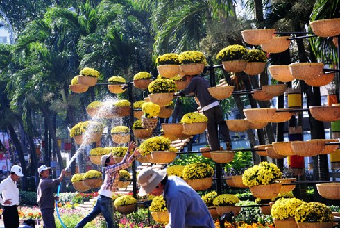 Sau những tuyến đường lớn như Đồng Khởi, Lê Duẩn, Lê Lợi, một số phố khác ở trung tâm thành phố cũng hoàn thành việc trang trí Tết. Đây là năm mà TP HCM có nhiều tuyến được thắp sáng bằng các dải đèn màu, theo từng chủ đề khác nhau. Thương xá Tax năm nay lấy màu hoa mai làm chủ đạo với ánh đèn đỏ, ấm vàng. Bên dưới là các trang trí Tết, từ 18h, rất đông người đến chụp ảnh và ngắm không khí xuân. Trong khi đó, từ các cửa hiệu lớn... ... đến các trung tâm thương mại, khách sạn bắt đầu trang trí bằng ánh sáng đủ màu. Đường hoa Nguyễn Huệ đang bước vào những ngày cuối cùng trước khi khai mạc sáng 27 tháng Chạp. Các biểu tượng năm rắn và quê hương đất nước đã gần hoàn thành. Những công nhân đang tưới các giò hoa treo cao. Mỗi chủ đề trên con đường hoa năm nay được dàn dựng bằng các hình ảnh mang cảnh sắc quen thuộc của Việt Nam. Rặng tre, ruộng lúa và khóm hoa xuất hiện giữa đường. Nhiều tuyến phố trung tâm thành phố được trang trí bằng đủ các loại hoa sặc sỡ. Tượng đài Hồ Chủ tịch trước UBND thành phố với sen chủ đạo và các cánh hoa màu sắc khác nhau. Các con thuyền hoa bên cạnh hồ Bán nguyệt, quận 7. Các hội chợ, lễ hội hoa đã diễn ra từ ngày 23 tháng Chạp. Năm nay, hoa từ các tỉnh miền Tây và phía Bắc chuyển về nhiều, mức giá vừa phải. Trong những ngày đầu mở cửa, lượng khách vãn cảnh nhiều, nhưng người mua ít.