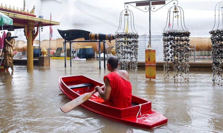 Nhà sư chèo thuyền cạnh một bức tượng Phật bị ngập trong nước lũ tại một ngôi chùa ở Ayutthaya, Thái Lan hôm 6-10