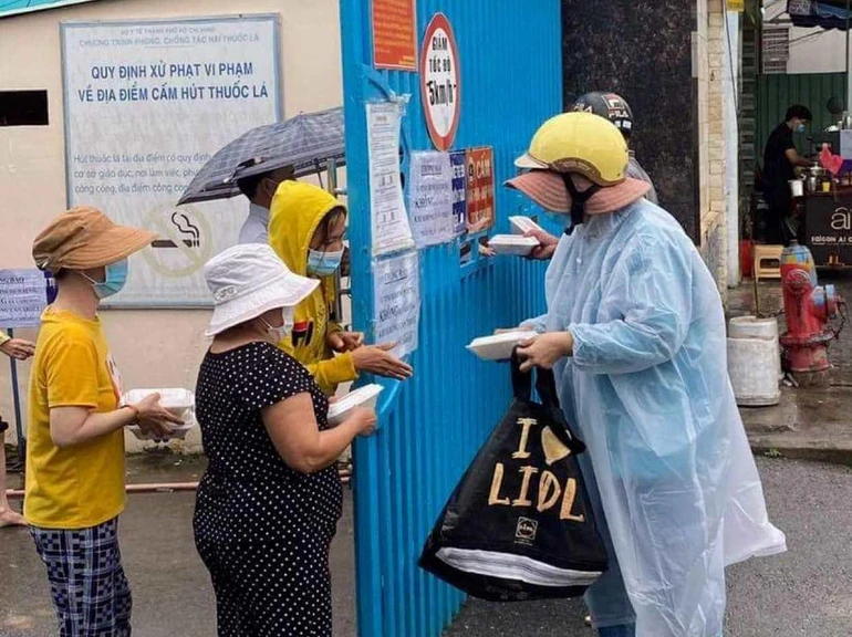 Tình nguyện viên tặng suất cơm chay đến thân nhân bệnh nhân tại cổng một bệnh viện - Ảnh: T.N