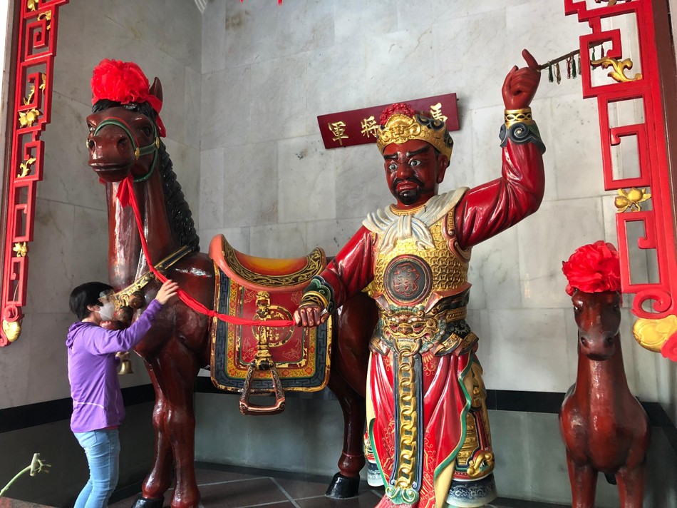 Một người Hoa nắm dây cương, rung lục lạc, vuốt thân ngựa Xích Thố và chui qua bụng nó để mong cầu may mắn tại &quot;chùa&quot; Ông (quận 5)