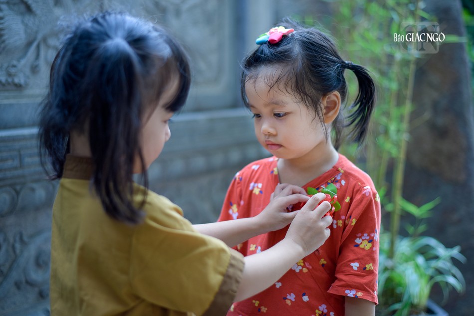 Bé Bông đang cài hoa hồng cho bạn của mình là bé Mịn