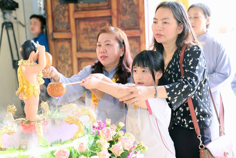Một em nhỏ cùng người thân thực hiện nghi thức Tắm Phật tại chùa Phước Viên
