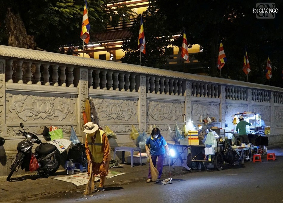 Hòa thượng Thích Duy Trấn cùng Phật tử rọi đèn để vệ sinh khu vực bên ngoài khuôn viên chùa, từ sáng sớm khi lát đát những quán hàng rong mới dọn hàng