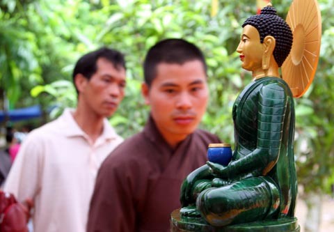 Tượng Phật ngọc tọa lạc trên đài sen trong ngôi chùa cổ miền Bắc. Hai ngày sau khi mở cửa tự do để người dân chiêm bái tượng Phật ngọc, lượng người kéo đến đây vẫn khá đông. Dù lượng người đến xem đông nhưng theo anh thanh niên này, ảnh tượng Phật ngọc bán không đắt hàng. "Xuống giá 10.000 đồng một ảnh to một ảnh nhỏ nhưng cũng chẳng mấy người mua. Từ sáng tới giờ tôi mới bán được chừng 300 tấm", người này nói. Tương tự, các cửa hàng bán tranh tượng Phật in trên gỗ, ảnh tượng Phật in trên đá... cũng ế ẩm. Trong khi đó, một công ty chuyên kinh doanh quà tặng đã chép nguyên mẫu tượng Phật ngọc để đúc lại với kích cỡ nhỏ hơn. Dù không phải làm thủ công mà được đúc bằng bột đá nhưng giá một bức tượng cao chừng 50 cm là 5 triệu đồng, còn bức tượng nhỏ bằng bàn tay giá 300.000 đồng. Loại tượng đặc biệt này đã thu hút sự chú ý của người xem. Tuy nhiên, nhiều người cũng chỉ dám cầm lên xem rồi đặt xuống... ... hay chụp bức ảnh làm kỷ niệm, thay vì chụp bức ảnh Phật ngọc nguyên mẫu được đặt ở quá xa. Dịch vụ chụp ảnh lấy ngay trong 5 phút cũng khá hút khách vì ai cũng muốn có một bức hình làm kỷ niệm nhân dịp tận mắt ngắm bức tượng Phật ngọc lớn nhất thế giới. Còn ở ngoài đường, mỗi khi có ôtô chở khách xịch đỗ là hàng chục người dân đi xe máy chạy tới mời đi xe ôm giá 10.000 - 15.000 đồng một lượt cho quãng đường 5-6 km. Nếu không đi xe ôm, du khách sẽ phải đi bộ vài km mới tới được nơi bày tượng Phật. Tượng Phật ngọc tọa lạc trên đài sen trong ngôi chùa cổ miền Bắc. Hai ngày sau khi mở cửa tự do để người dân chiêm bái tượng Phật ngọc, lượng người kéo đến đây vẫn khá đông. Dù lượng người đến xem đông nhưng theo anh thanh niên này, ảnh tượng Phật ngọc bán không đắt hàng. "Xuống giá 10.000 đồng một ảnh to một ảnh nhỏ nhưng cũng chẳng mấy người mua. Từ sáng tới giờ tôi mới bán được chừng 300 tấm", người này nói. Tương tự, các cửa hàng bán tranh tượng Phật in trên gỗ, ảnh tượng Phật in trên đá... cũng ế ẩm. Trong khi đó, một công ty chuyên kinh doanh quà tặng đã chép nguyên mẫu tượng Phật ngọc để đúc lại với kích cỡ nhỏ hơn. Dù không phải làm thủ công mà được đúc bằng bột đá nhưng giá một bức tượng cao chừng 50 cm là 5 triệu đồng, còn bức tượng nhỏ bằng bàn tay giá 300.000 đồng. Loại tượng đặc biệt này đã thu hút sự chú ý của người xem. Tuy nhiên, nhiều người cũng chỉ dám cầm lên xem rồi đặt xuống... ... hay chụp bức ảnh làm kỷ niệm, thay vì chụp bức ảnh Phật ngọc nguyên mẫu được đặt ở quá xa. Dịch vụ chụp ảnh lấy ngay trong 5 phút cũng khá hút khách vì ai cũng muốn có một bức hình làm kỷ niệm nhân dịp tận mắt ngắm bức tượng Phật ngọc lớn nhất thế giới. Còn ở ngoài đường, mỗi khi có ôtô chở khách xịch đỗ là hàng chục người dân đi xe máy chạy tới mời đi xe ôm giá 10.000 - 15.000 đồng một lượt cho quãng đường 5-6 km. Nếu không đi xe ôm, du khách sẽ phải đi bộ vài km mới tới được nơi bày tượng Phật.